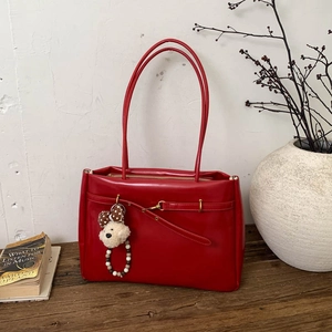Close-up of red minimalist tote bag with thin straps and cute teddy bear charm on wood
