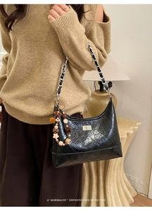 Detail of black quilted shoulder bag with silver chain strap and colorful beaded charm