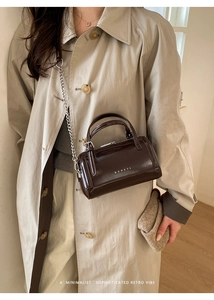 Detail of a dark brown oil wax leather Boston bag with silver chain and brand logo