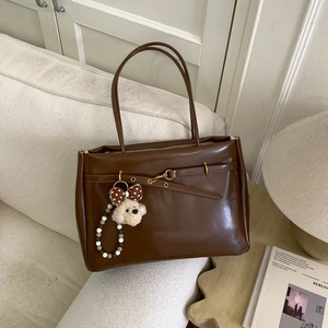Detail of brown faux leather tote bag with decorative metal buckle and plush bear charm