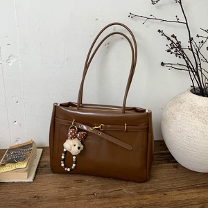 Close-up of brown leather tote bag with metal buckle and cute plush dog pendant charm