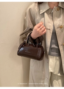 Détail du sac Boston en cuir brillant marron foncé avec logo MUHETI et deux poignées