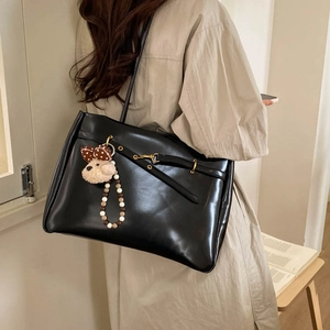 Macro detail of glossy black leather tote bag with golden hardware and plush charm