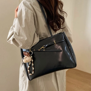 Detail of a large black leather tote bag with a cute bear charm and golden buckle accents