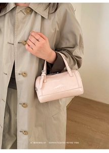 Détail d'un sac cylindrique rose brillant avec logo embossé et fermeture éclair argentée