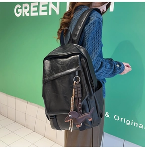 Close-up of black leather backpack featuring a cute brown dachshund charm and stylish accessories
