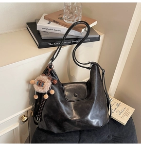 Detail of a vintage black leather hobo bag with a cute plush sheep charm and magnetic flap