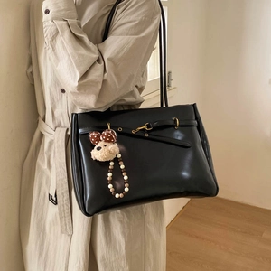 Detail of black leather tote bag with decorative strap, gold buckle and cute bear charm