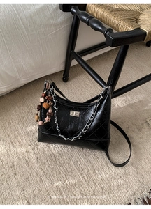 Detail of black quilted leather bucket bag with silver chain and colorful bead charm