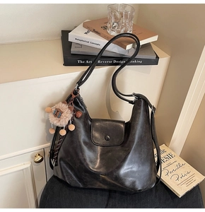 Detail of a black leather hobo shoulder bag with a cute plush charm on a black stool