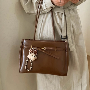 Detail of dark brown leather tote bag with gold buckle and cute puppy plush charm accessory
