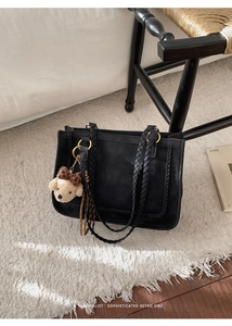 Detail of black suede tote bag featuring woven handles and a cute plush bear charm