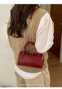 Mannequin portant un sac cylindre en cuir verni rouge foncé avec chaîne argentée