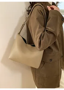Bolso tipo cubo en cuero beige con patrón litchi en el hombro de la modelo