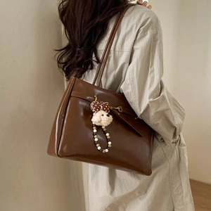 Detail view of large dark brown leather tote bag with a cute bear charm on shoulder
