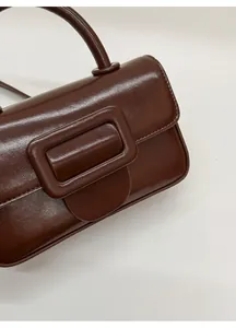 Detail view of a vintage dark brown leather handbag with rectangular buckle and firm handle