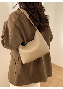 Detalle del bolso tipo cubo de cuero granulado beige llevado con un elegante abrigo marrón