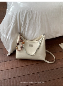 Detailed shot of cream quilted shoulder bag with silver chain and beaded charm on wood floor