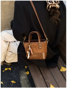 Detail of brown contrast leather crossbody bag with beaded pendant and shoulder strap