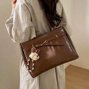 Detail of vintage dark brown faux leather tote bag with teddy bear charm on shoulder