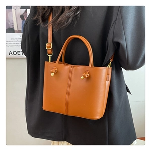 Damen Eimertasche in Tan mit Knoten-Detail aus Goldmetall am Modell in schwarzem Anzug