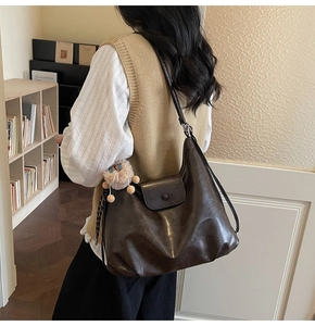 Detail view of large dark brown leather hobo bag with flap and plush charm on shoulder