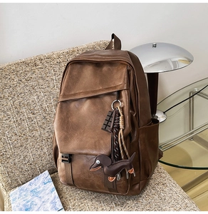 Detailed view of vintage brown leather backpack with multiple cute charms on beige sofa
