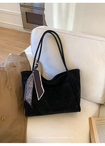 Detail of black suede tote bag featuring a decorative polka dot silk scarf on a white sofa