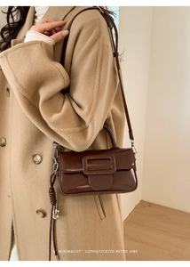 Detail view of dark brown patent leather square bag with large buckle on wool coat