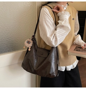 Detail view of large dark brown leather shoulder bag with cute plush lion charm
