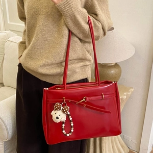 Detail of red high-gloss leather tote bag featuring a cute white puppy plush charm