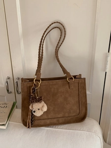 Brown suede tote bag with woven details and charm pendant in a retro interior setting