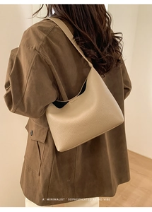 Bolso hobo beige minimalista con textura granulada llevado por modelo con abrigo marrón