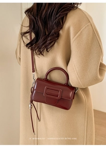 Close-up of a burgundy glossy handbag with square buckle and slender strap detail