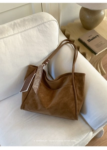 Brown leather tote bag with decorative floral scarf on a minimalist white sofa