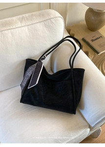 Detail of black suede tote bag with a decorative polka dot scarf on a soft sofa