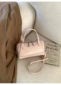 Close-up of pale pink Boston bag featuring embossed logo and silver metallic zippers