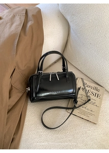 Close-up of black leather Boston bag with silver zipper and MUHETI logo on white sofa
