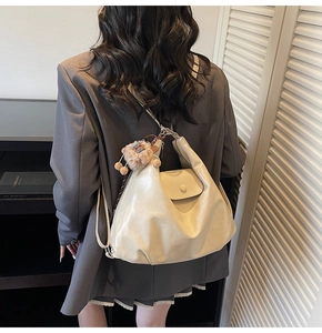 Close-up of beige glossy hobo bag with vintage pocket and brown plush monster charm