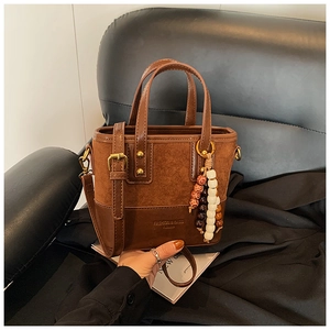 Detail of dark brown leather bucket bag with suede texture and beaded tassel charm