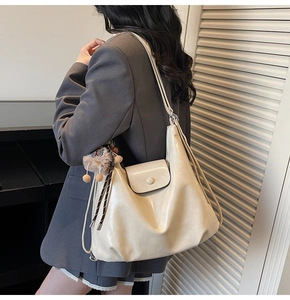 Detail view of large cream leather tote bag with flap closure and cute plush charm
