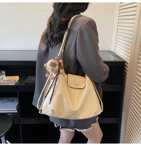 Macro detail of cream leather tote bag featuring a cute plush lion charm and wide strap
