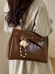 Brown retro tote bag with plush puppy charm worn by model over shoulder