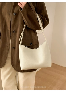 Primer plano de un bolso de hombro de cuero granulado blanco sobre un abrigo marrón