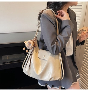 Detail of cream white faux leather hobo bag with round buckle and plush charm on grey suit