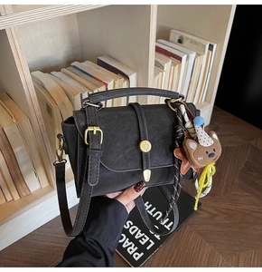 Detalle de bolso bandolera retro negro con hebilla dorada y amuleto de oso pardo
