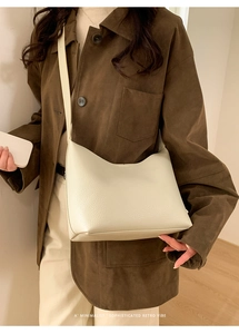 Bolso tipo cubo minimalista de cuero granulado beige llevado por modelo en un interior