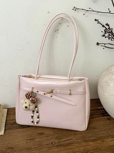 Pink PU leather tote bag with gold buckle and dog charm on a rustic wooden table