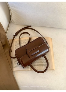 Detail of dark brown leather handbag with rectangular buckle on an open book background