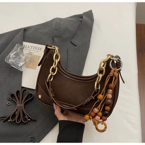 Detail of dark brown saddle bag with golden chain handle and ethnic wooden bead pendant
